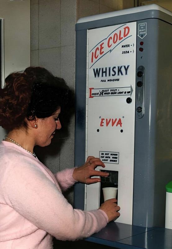 [colorized] A woman trying the new Office Whiskey Machine at the Second Automatic Vending Exhibition in London, England. (February 1960)